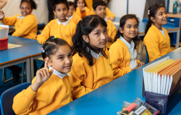 Girls in a classroom, with one raising her hand