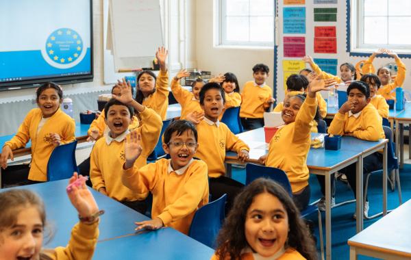 Children in a classroom, raising their hands