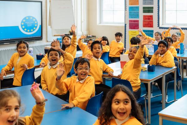 Children in a classroom, raising their hands